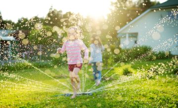 Adorable little girls playing with a sprinkler in a backyard on sunny summer day. Cute children having fun with water outdoors.