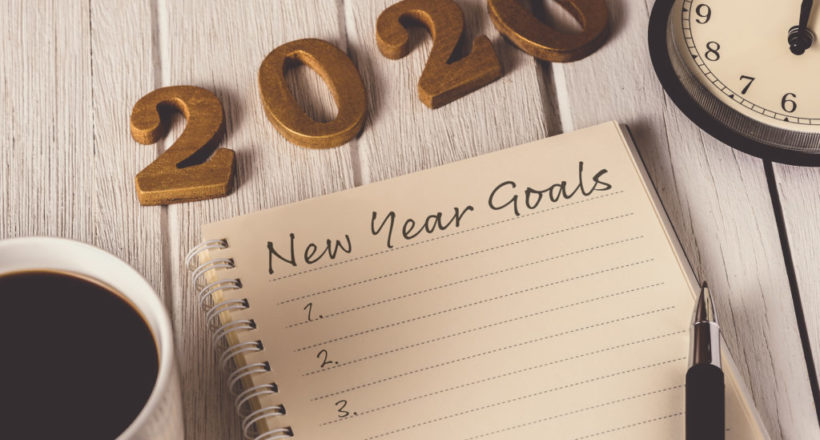 New Year's Goals List written on Notebook with alarm clock, pen, coffee