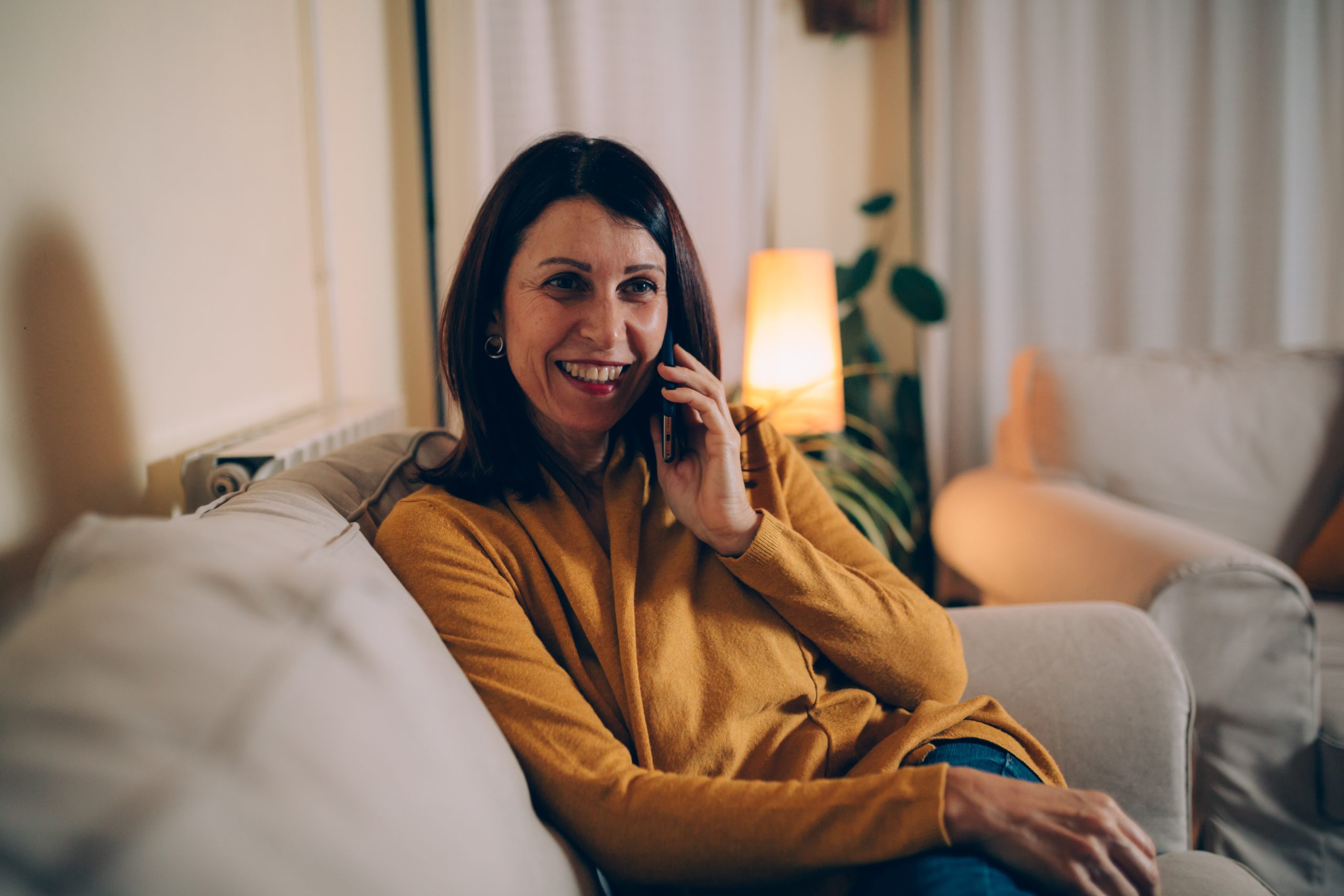 woman sitting sofa at home talking on mobile phone