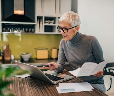 Portrait of a senior woman working with laptop and documents in the kitchen.