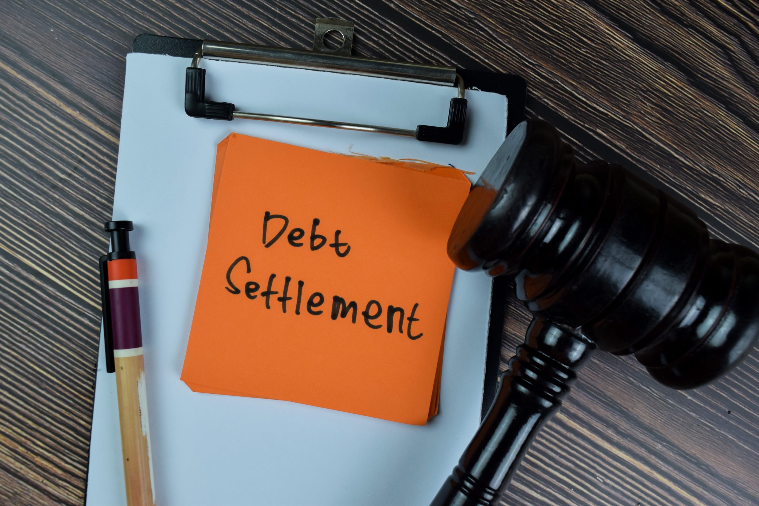 Concept of Debt Settlement write on sticky notes with gavel isolated on Wooden Table.