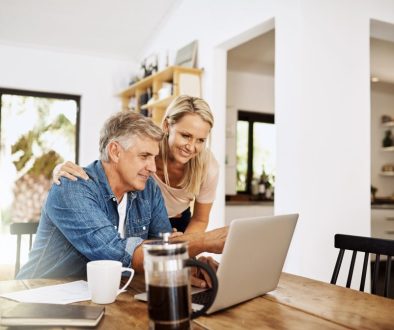 Couple with laptop planning finance, banking and checking retirement budget while becoming debt free at home. Smiling, happy and cheerful mature man showing woman an approved bank loan on technology