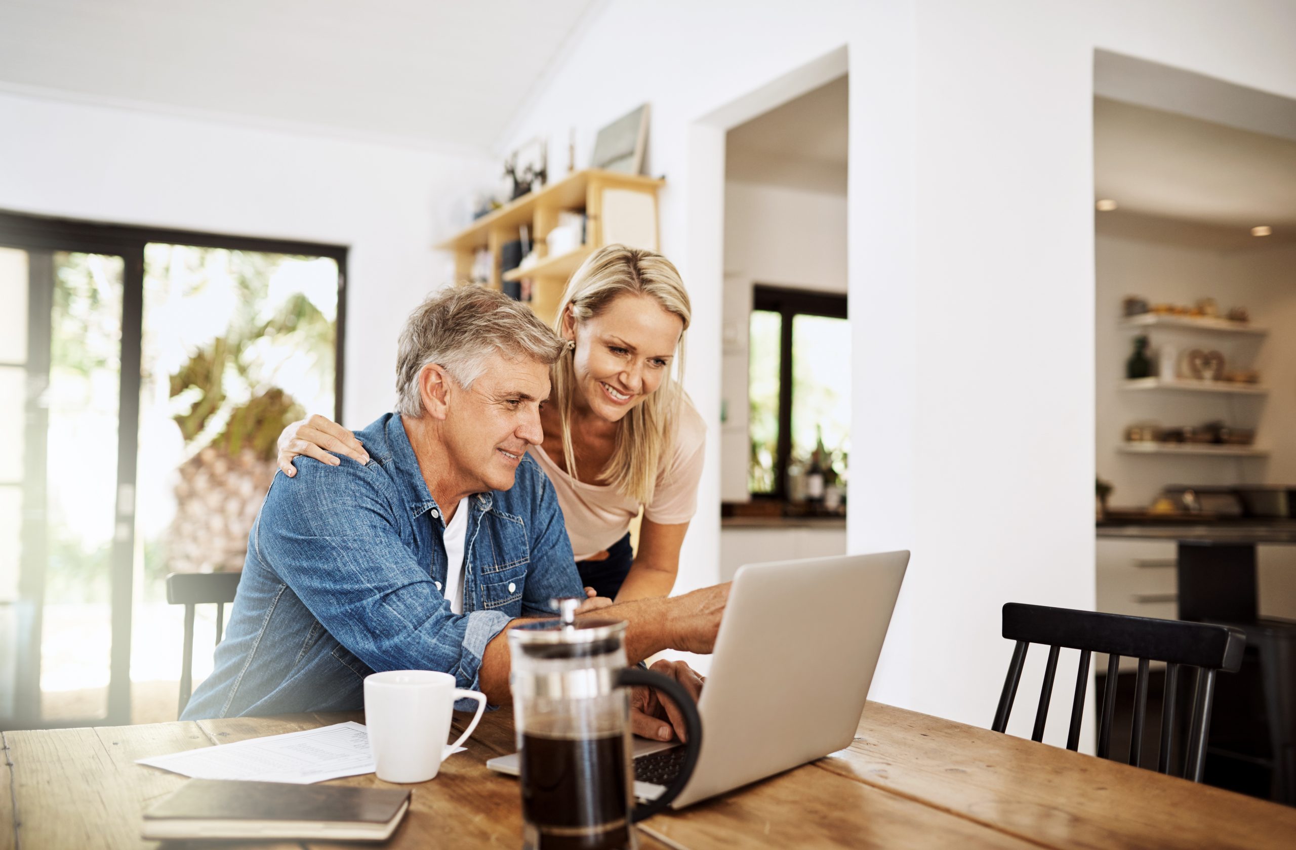 Couple with laptop planning finance, banking and checking retirement budget while becoming debt free at home. Smiling, happy and cheerful mature man showing woman an approved bank loan on technology