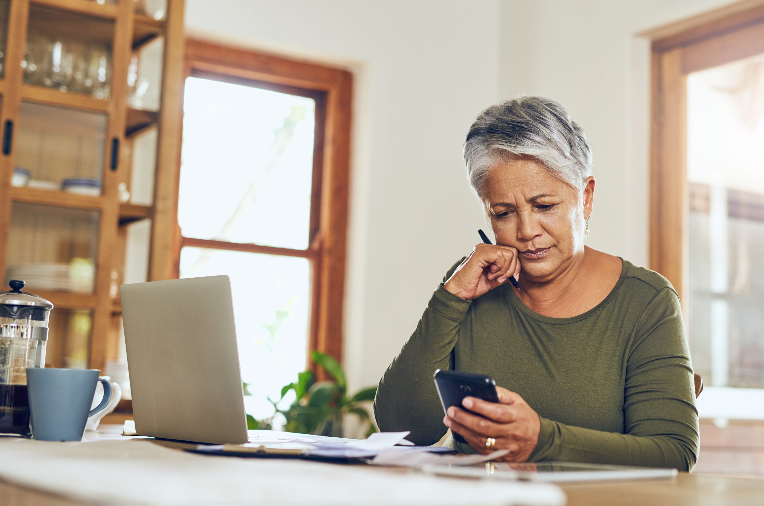 Senior woman, phone budget planning and health insurance checklist at home. Writing, contract and elderly female person with mobile banking, tax and pension form in a house with bills and debt